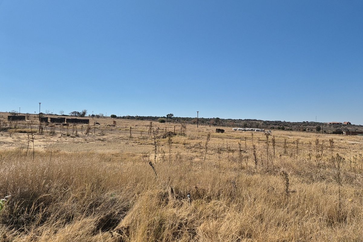 A wide-angle view of a vacant residential plot featuring dry grass and utility poles under a clear blue sky.