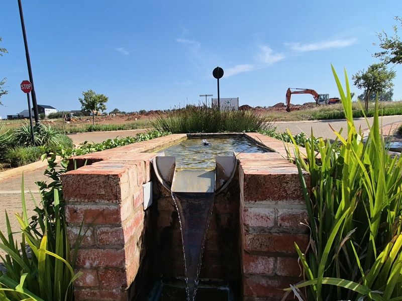 A decorative brick water feature set within a landscaped garden area, overlooking a developing residential estate with construction activity in the background.