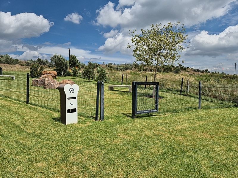 A well-maintained fenced dog park area featuring a lawn, concrete seating, and a dedicated pet waste disposal station.