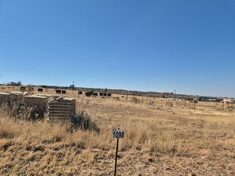 A view of a vacant residential plot featuring dry grass and a property boundary marker.