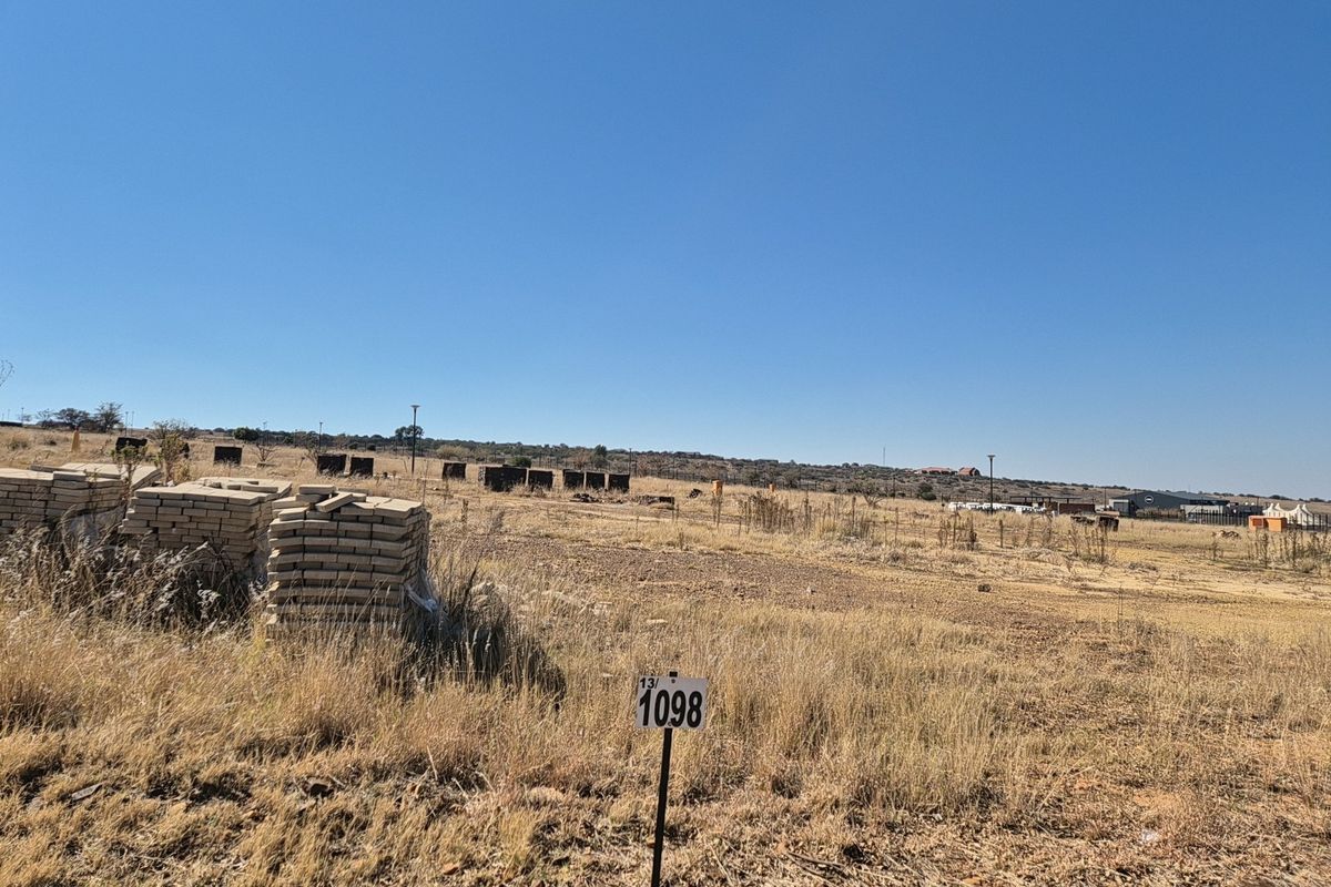 A view of a vacant residential plot featuring dry grass and a property boundary marker.