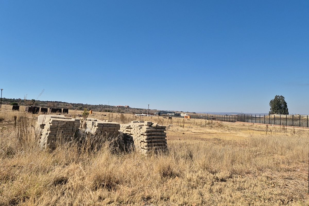 A vacant residential plot featuring dry grass, perimeter fencing, and stacks of building materials, offering a clear view of the surrounding landscape.