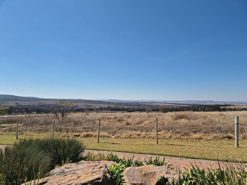 A scenic view of the expansive landscape featuring a well-maintained garden, paved walkway, and post and rope fencing.