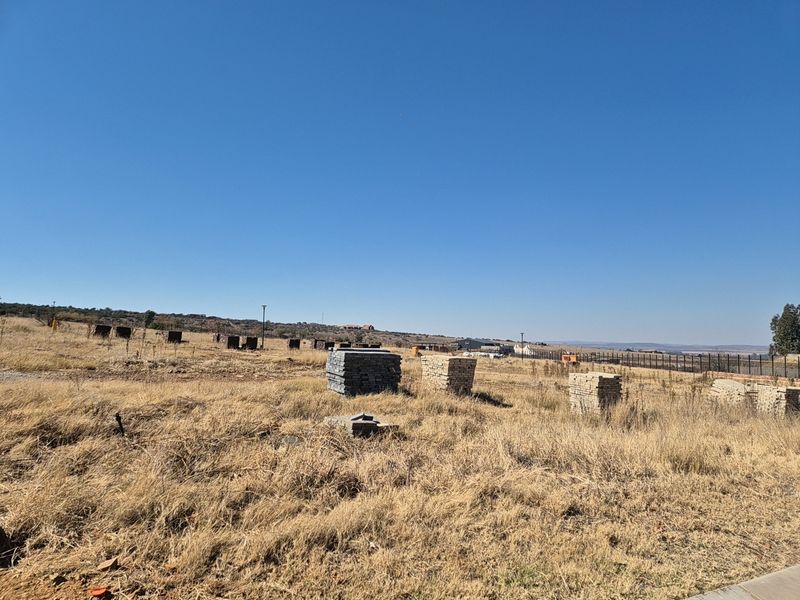 A vacant residential plot featuring dry grass, open space, and perimeter fencing, offering a clear view of the surrounding landscape.