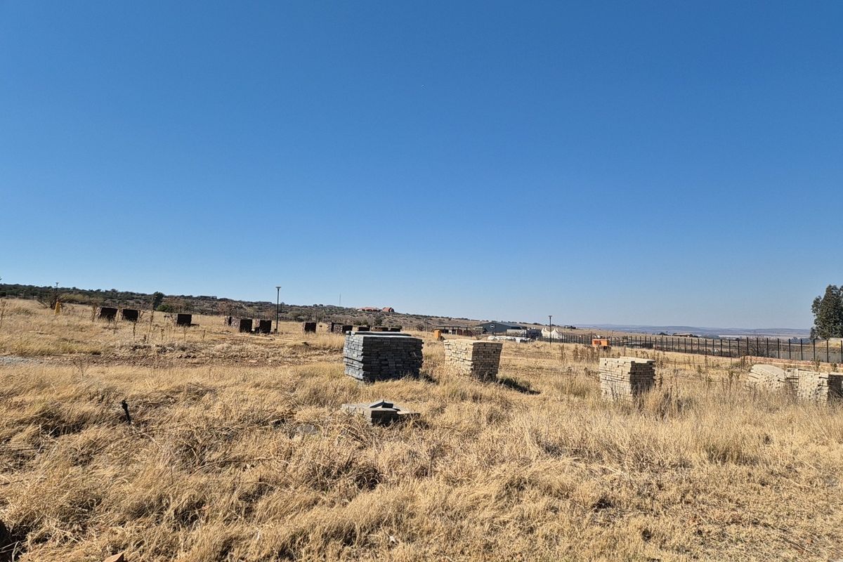A vacant residential plot featuring dry grass, open space, and perimeter fencing, offering a clear view of the surrounding landscape.