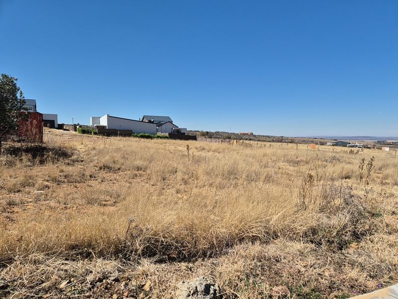 A view of a vacant residential plot featuring dry grass and surrounding neighborhood development.