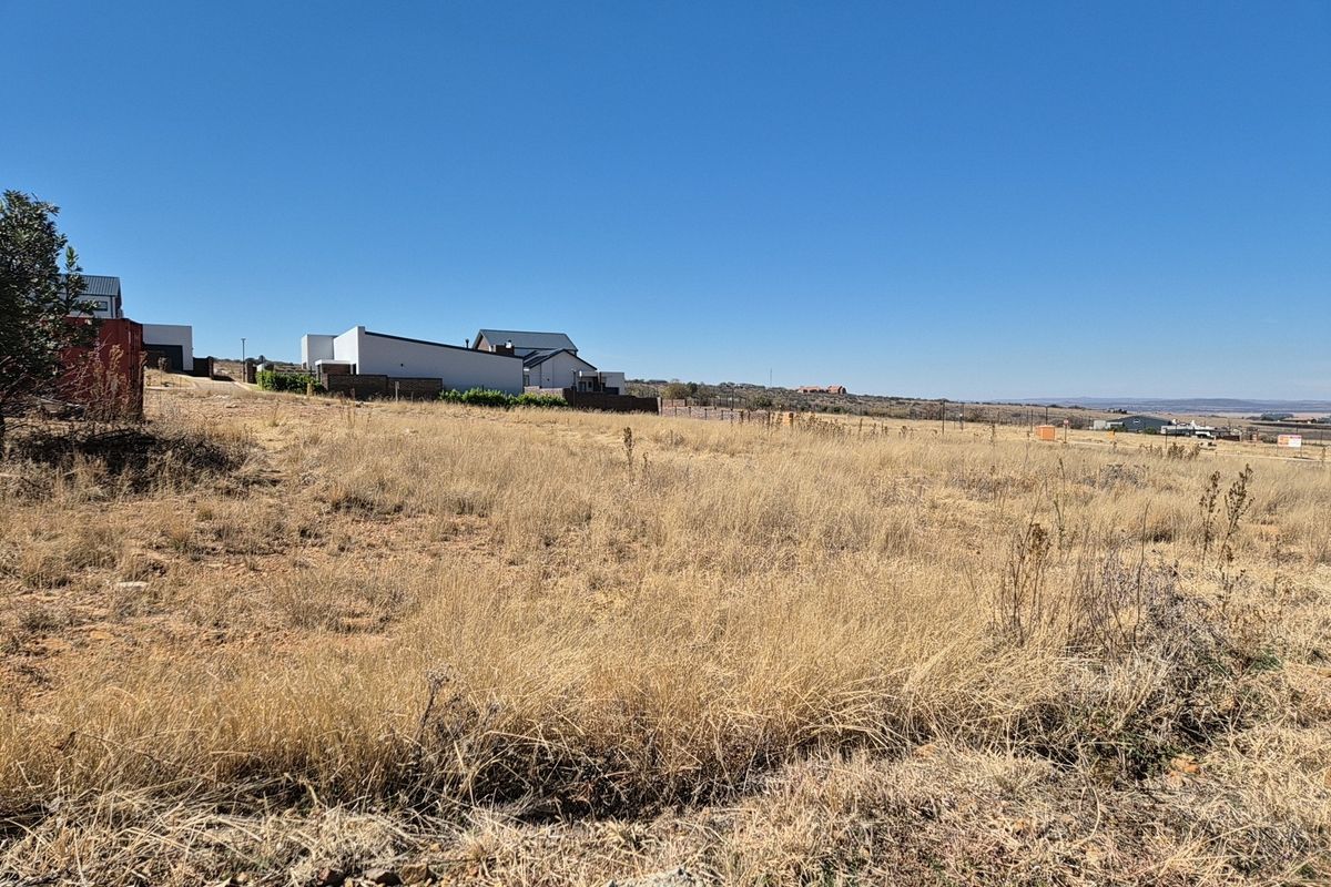 A view of a vacant residential plot featuring dry grass and surrounding neighborhood development.