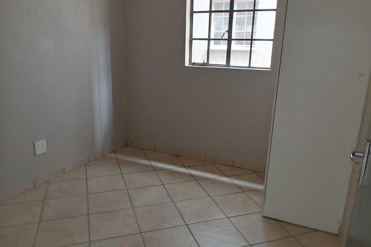 An empty bedroom featuring neutral tiled flooring, a built-in cupboard, and a steel-framed window providing natural light.
