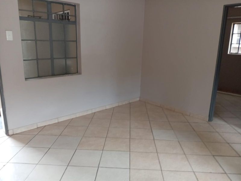An empty living area featuring neutral tiled flooring and a steel-framed window, providing a blank canvas for interior design.