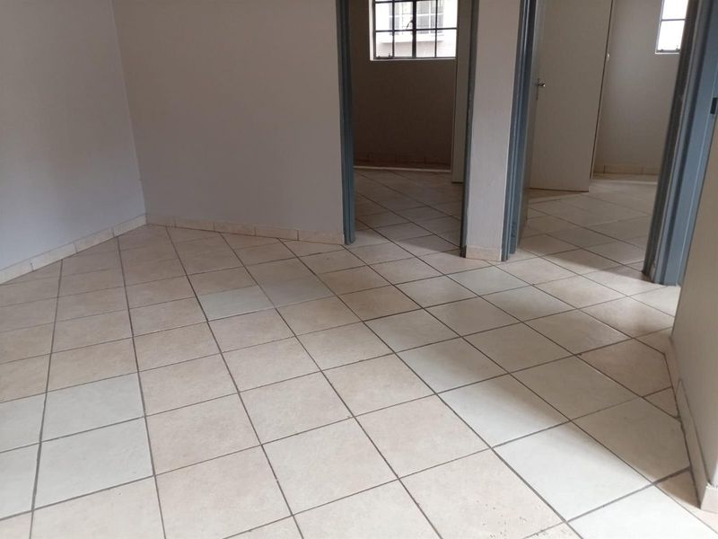 An empty living area featuring neutral ceramic floor tiles and access to adjacent rooms through standard internal doorways.