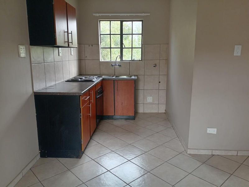 A functional kitchen featuring built-in cabinetry, a double basin sink, an electric hob, and tiled flooring, offering a clean and practical workspace.