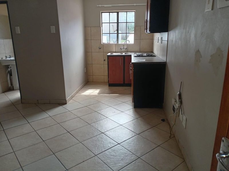 A compact, empty kitchen featuring tiled flooring, built-in cabinetry, a hob, and a tiled splashback, requiring some cosmetic wall repairs.