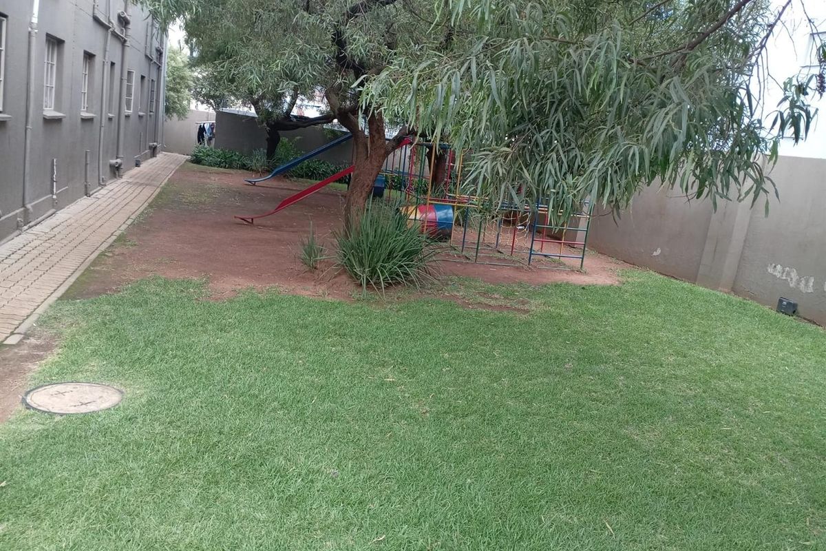 A communal rear garden area featuring a lawn, paved walkway, and mature trees, providing an outdoor space for residents.