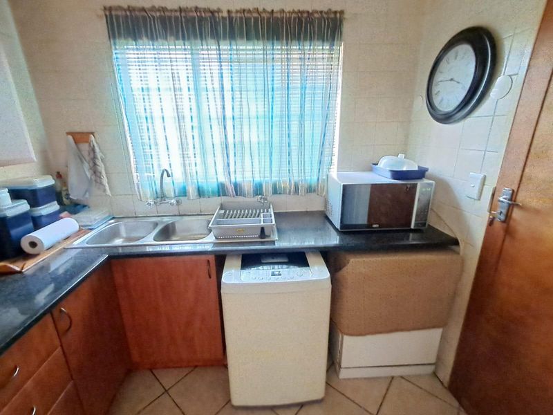 A functional laundry area featuring a double sink, dark granite countertops, and built-in wooden cabinetry with space for a top-loading washing machine.