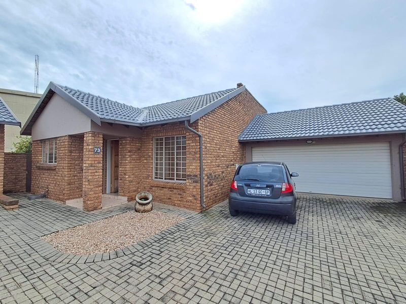 Front elevation of a face-brick townhouse featuring a tiled roof, paved driveway, and an integrated single garage.