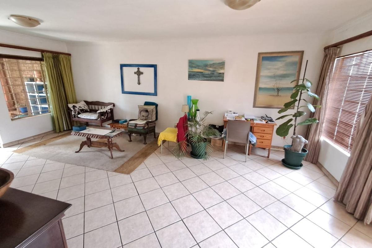 Spacious living area featuring neutral ceramic floor tiles, large windows with blinds, and direct access to an outdoor patio space.