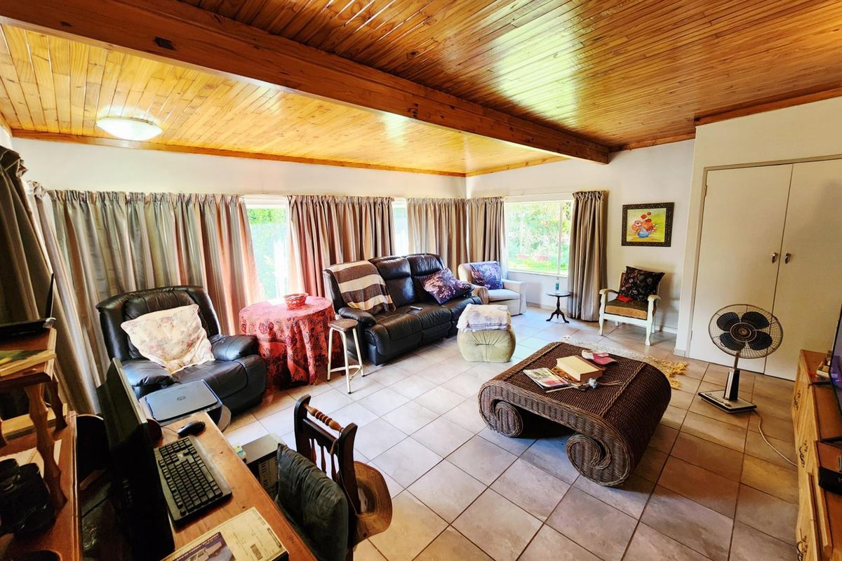 Spacious living room featuring a high timber-paneled ceiling, tiled flooring, and large windows providing natural light.