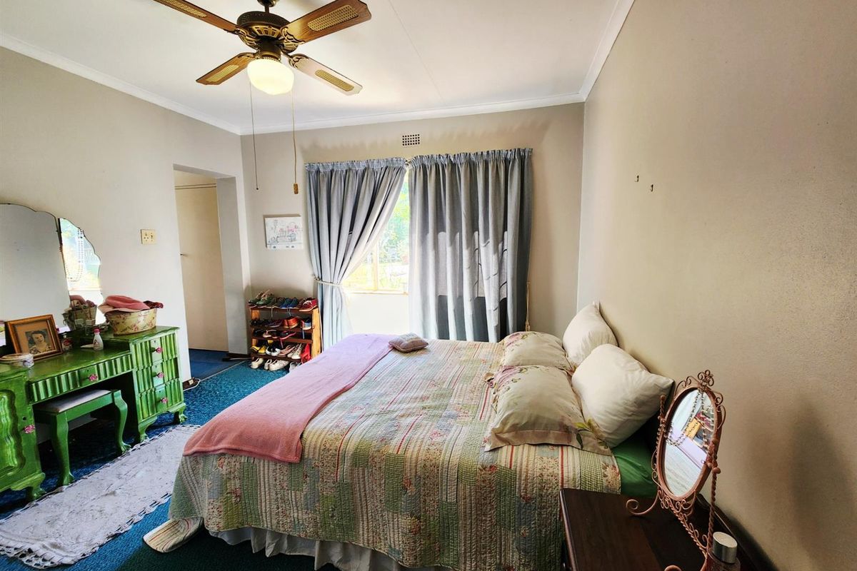 A bedroom featuring a ceiling fan, carpeted flooring, and natural light through a window with curtains.