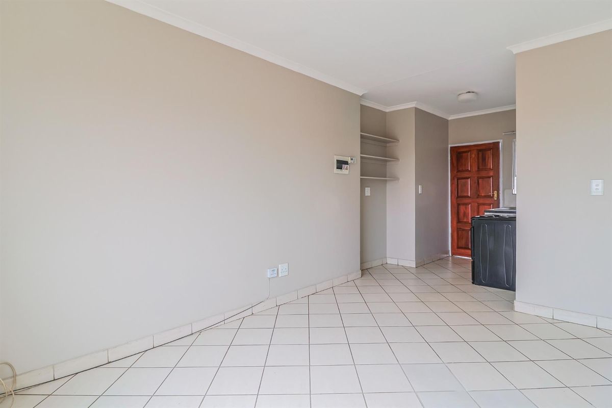 An empty living area featuring neutral walls, tiled flooring, and built-in shelving, leading to a timber entrance door.