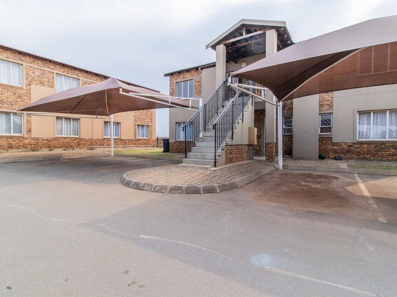 Exterior view of an apartment complex featuring paved parking bays with shade sails and an external staircase leading to upper-level units.