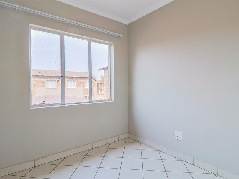 A clean, empty bedroom featuring neutral wall paint, tiled flooring, and a large window providing natural light.
