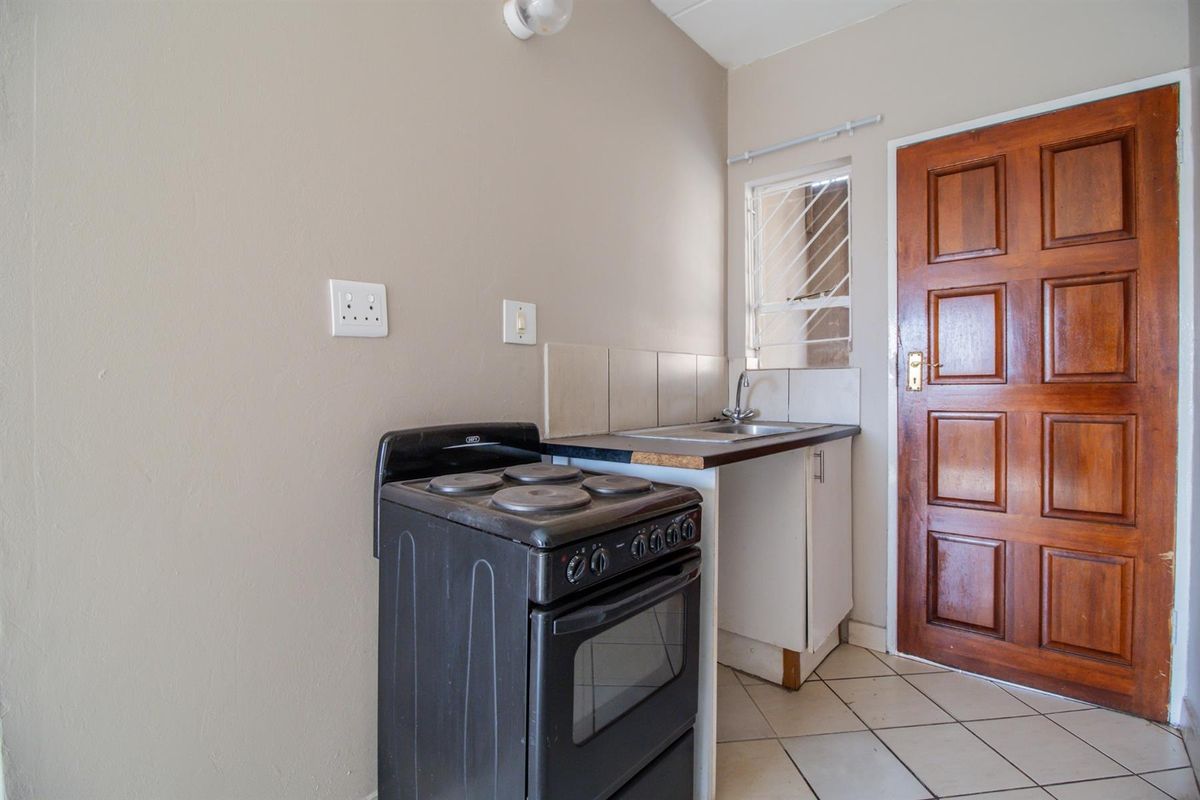 A compact kitchen area featuring a freestanding stove, sink with tiled splashback, and tiled flooring, providing a functional space for culinary needs.