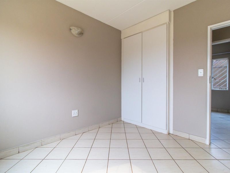 A clean, empty bedroom featuring neutral wall tones, tiled flooring, and a built-in wardrobe, offering a versatile space ready for personalization.