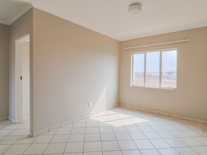 A bright, empty bedroom featuring neutral wall tones, tiled flooring, and a large window providing natural light.
