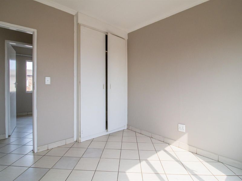 An empty bedroom featuring neutral wall paint, ceramic floor tiles, and a built-in wardrobe with sliding doors.