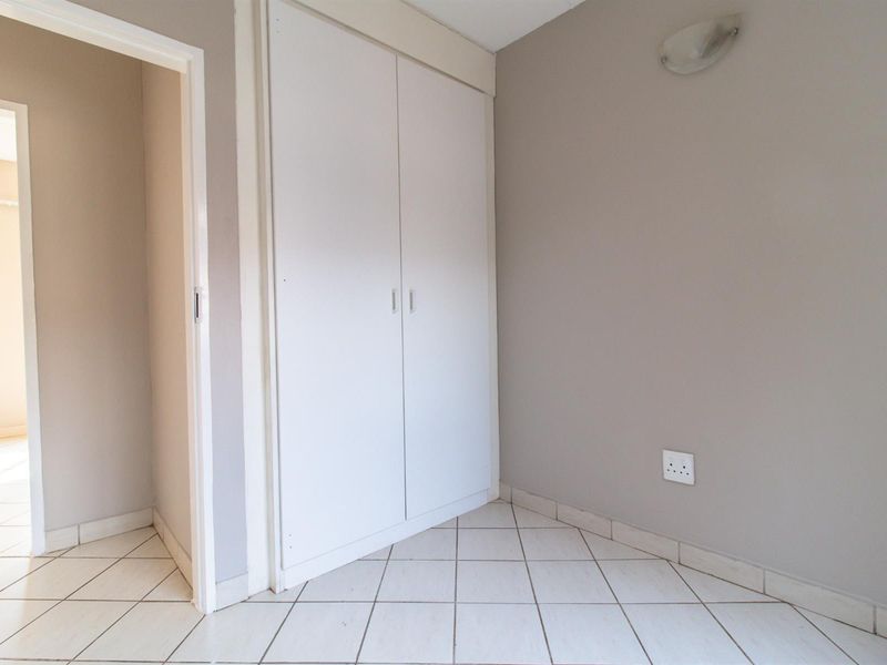 An empty bedroom featuring neutral wall paint, tiled flooring, and a built-in cupboard, offering a clean and versatile space.