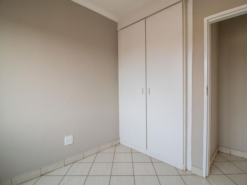 A clean, empty bedroom featuring neutral wall tones, tiled flooring, and a built-in wardrobe with white doors.