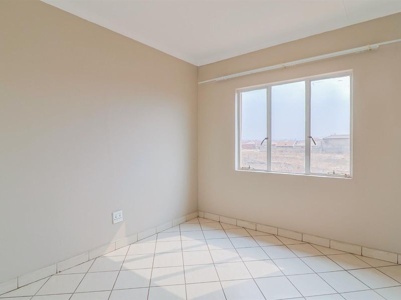 A bright, empty bedroom featuring neutral wall paint, tiled flooring, and a window with a curtain rail.
