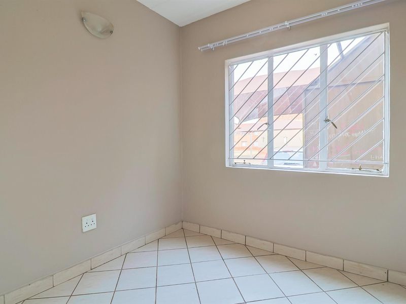 A clean, empty bedroom featuring neutral wall paint, tiled flooring, and a window fitted with security bars.