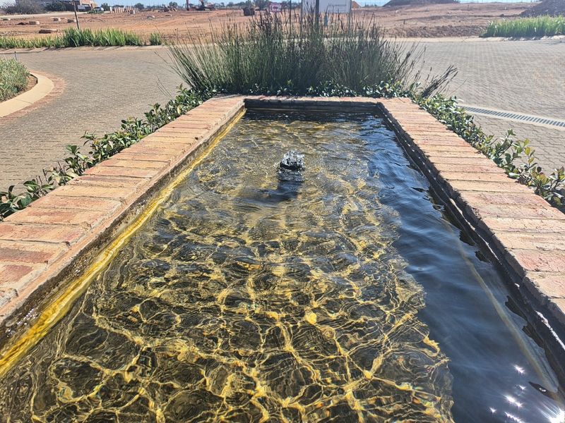 A decorative brick water feature with a central fountain located within a landscaped residential estate area.
