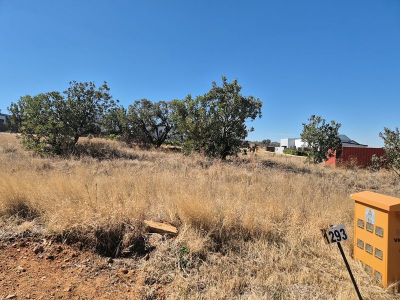 A vacant residential plot featuring natural vegetation, mature trees, and a visible electrical utility connection point.