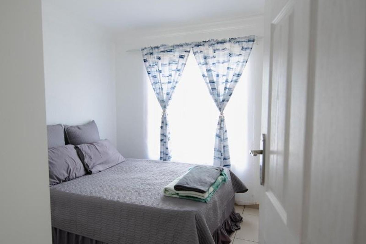 A compact bedroom featuring neutral floor tiles, a window with curtain tracks, and a central ceiling light fixture.