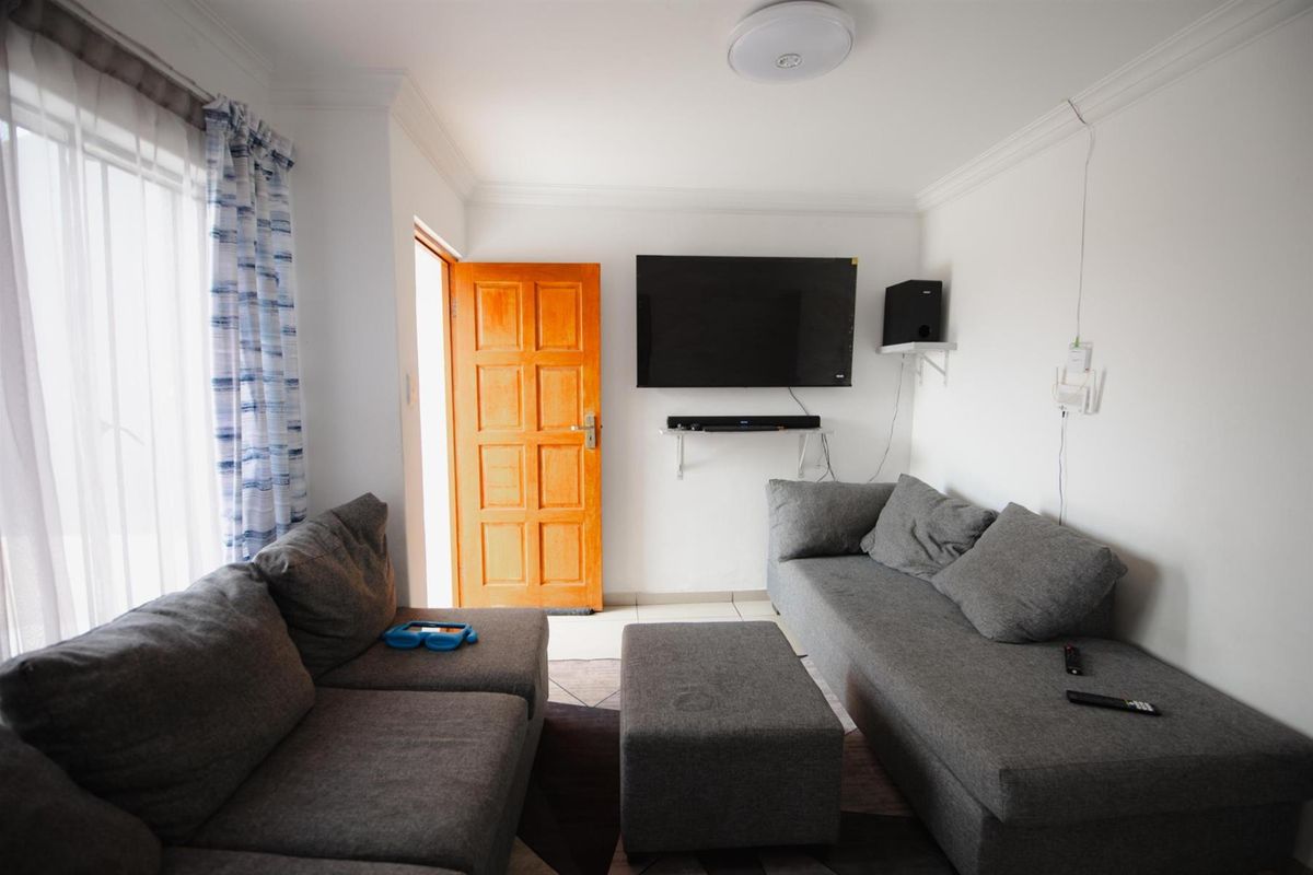 A functional living room featuring tiled flooring, a ceiling-mounted light fixture, and a wooden door leading to an exterior space.