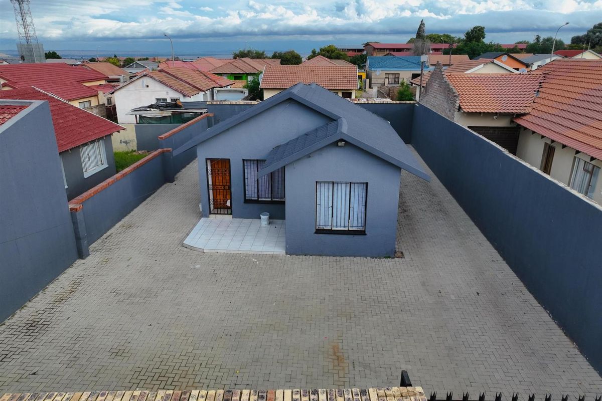 Aerial view of a detached house featuring a paved driveway, perimeter boundary walls, and a tiled entrance porch.