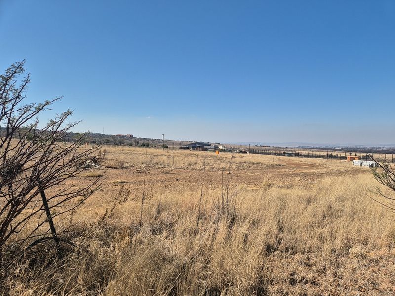 A wide-angle view of a vacant residential plot featuring dry grass and perimeter fencing under a clear blue sky.
