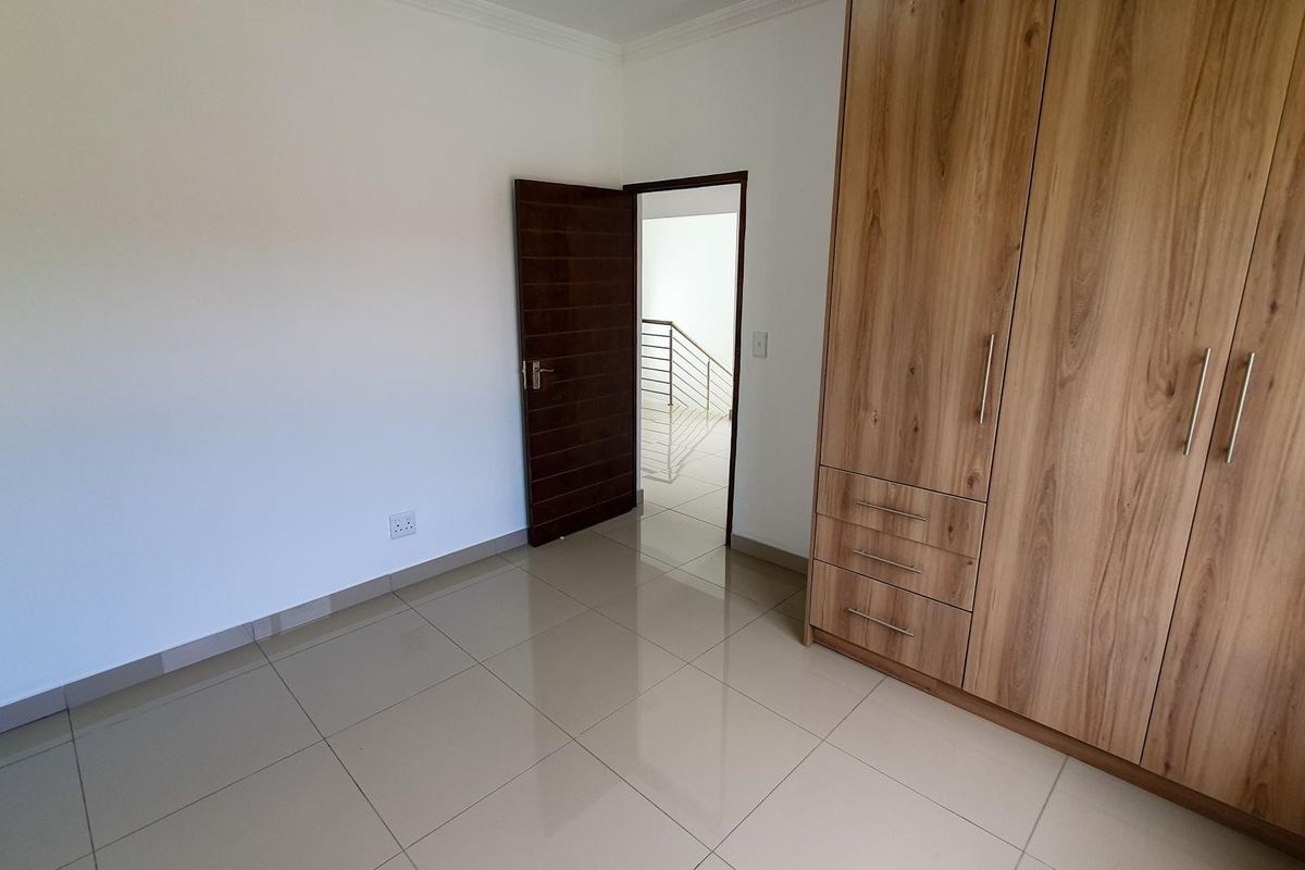 A bright bedroom featuring neutral tiled flooring and built-in wooden cabinetry, providing ample storage space and a clean, modern aesthetic.