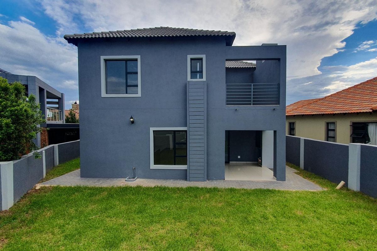 Rear view of a modern two-story house featuring a covered patio, upper-level balcony, tiled flooring, and a private enclosed garden.