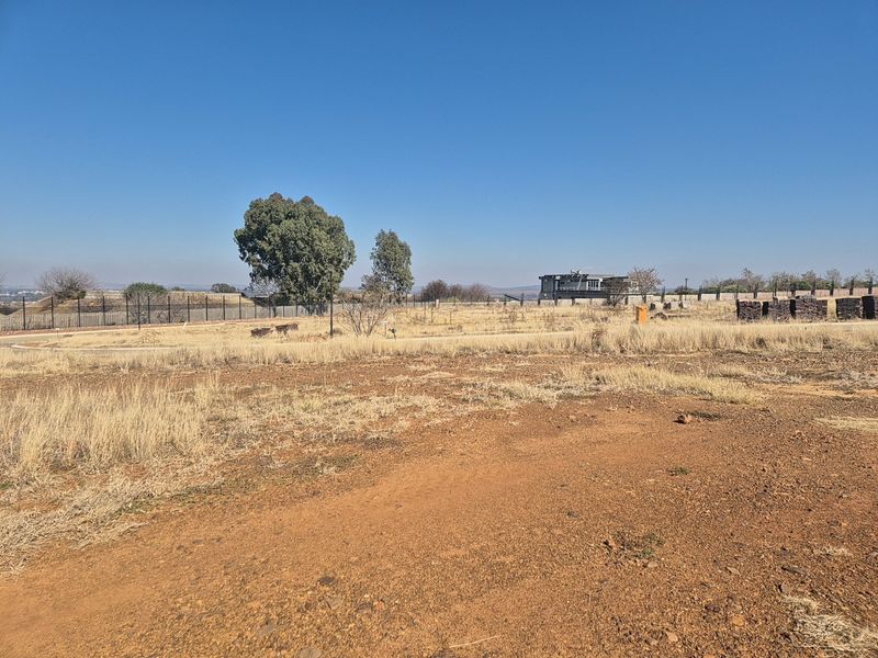 A vacant residential plot featuring dry grass, perimeter fencing, and clear road access, offering a blank canvas for future development.