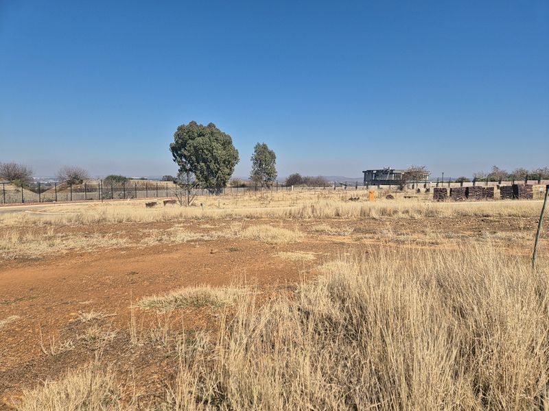 A vacant residential plot featuring dry grass, perimeter fencing, and open space, ready for development.