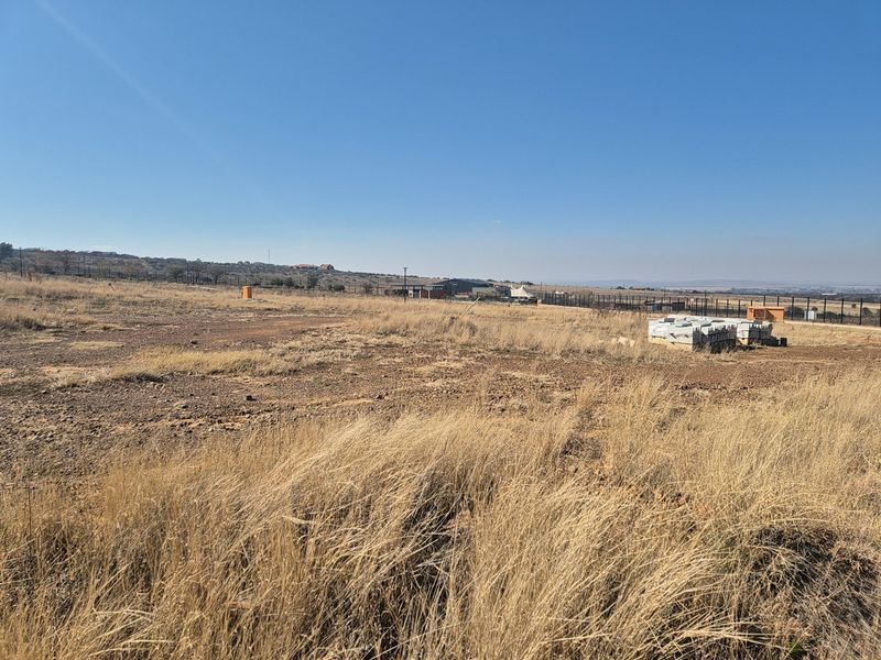 A wide-angle view of a vacant residential plot featuring dry grass, perimeter fencing, and clear horizon views.