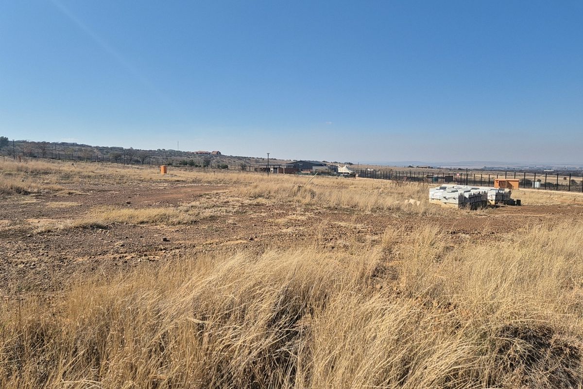A wide-angle view of a vacant residential plot featuring dry grass, perimeter fencing, and clear horizon views.