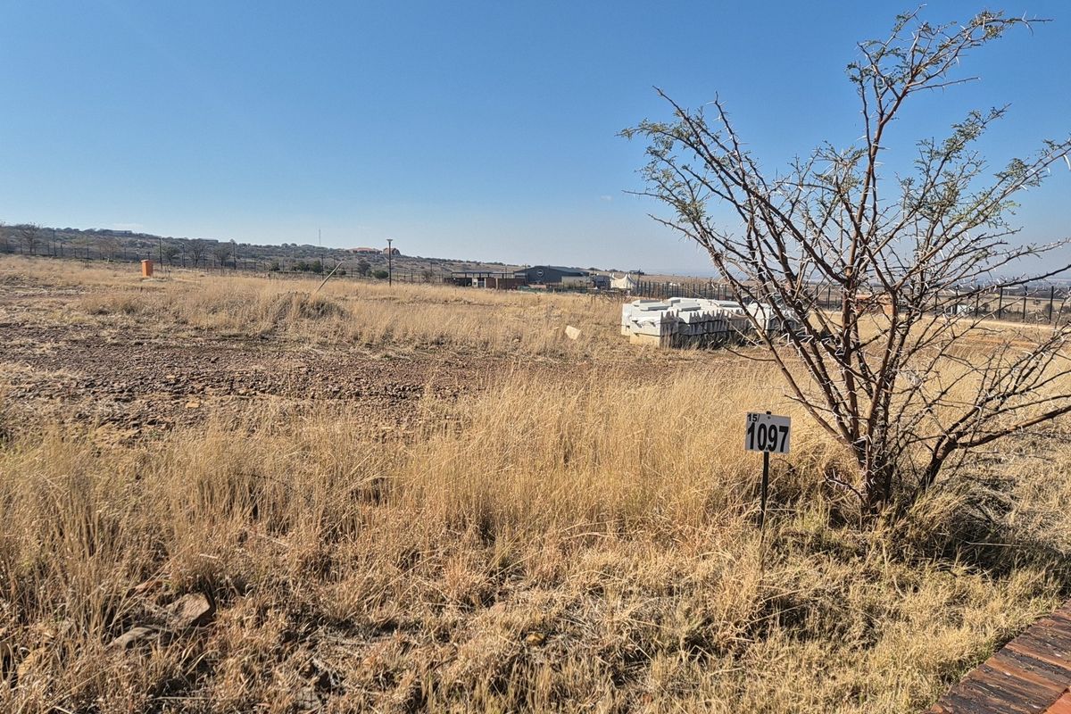 A view of a vacant residential plot featuring dry grass, native vegetation, and perimeter fencing, suitable for future development.