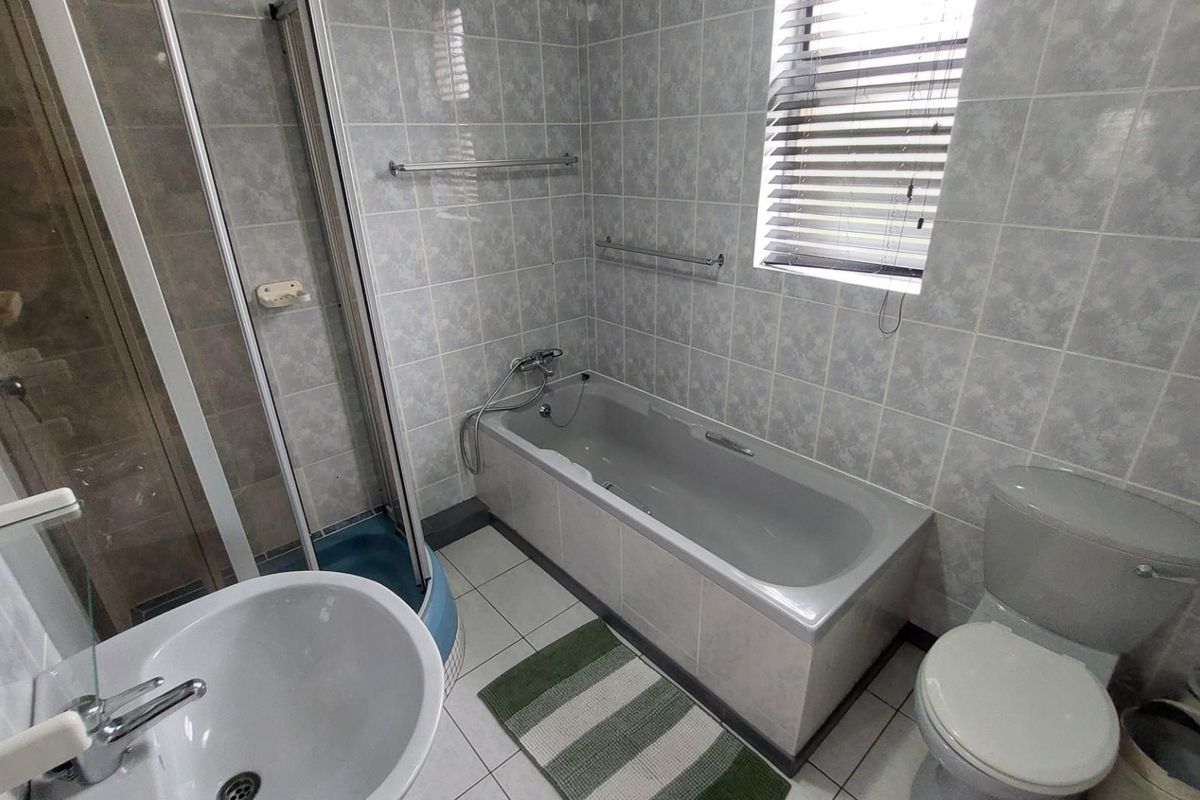 A functional bathroom featuring a bathtub, separate shower enclosure, pedestal basin, and toilet with neutral wall tiling and a window for natural light.