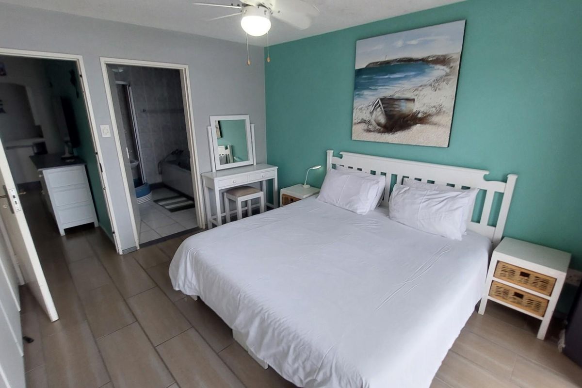 A well-lit bedroom featuring tiled flooring, a ceiling fan, and an en-suite bathroom access.