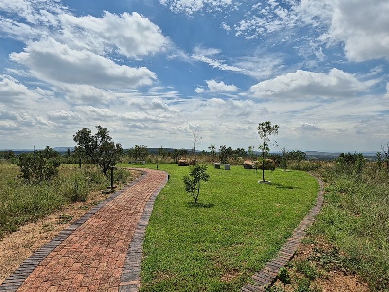 A well-maintained garden area featuring a curved brick paved pathway, manicured lawn, and natural stone landscaping elements with expansive open views.
