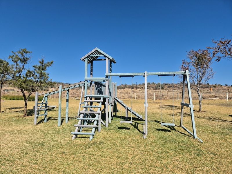 A residential garden featuring a wooden playground structure with swings and a slide set on a maintained lawn.